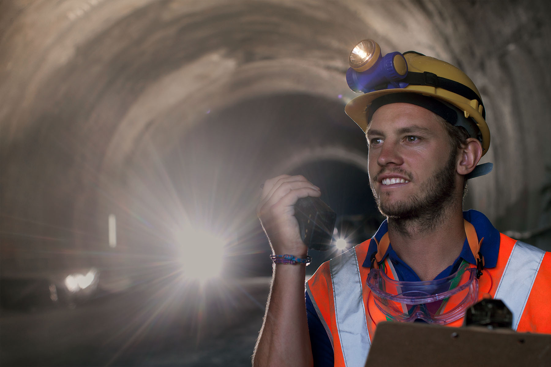 Bauarbeiter mit Helm steht in einem Tunnel und hält ein Walkie-Talkie in der Hand.